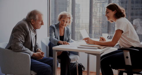 A young professional assists an elderly couple with paperwork in a modern office setting.