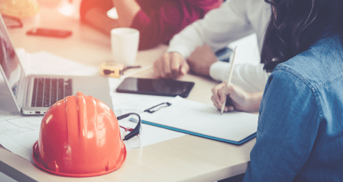 Woman taking notes at a meeting with construction hard hat on table.