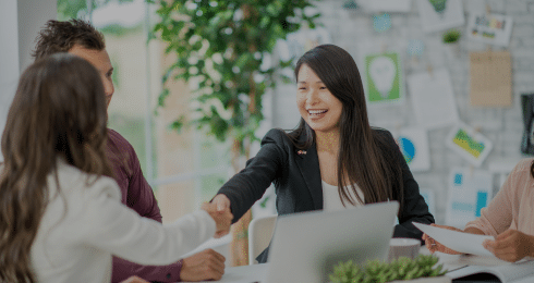 Group meeting with woman in a black blazer smiling and shaking hands in an office setting.