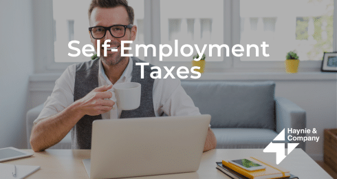 Man sipping coffee while working on self-employment taxes at a laptop.