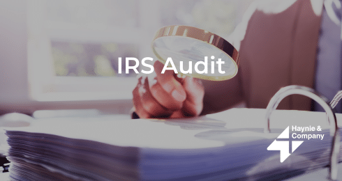 IRS audit concept with person examining documents through a magnifying glass, Haynie logo.