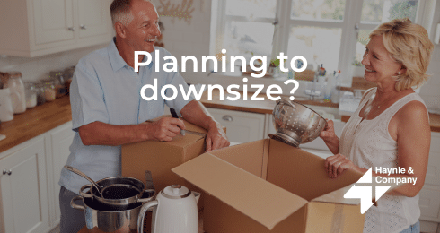 Elderly couple packing kitchen items in a box, discussing downsizing plans.