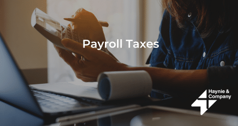 A person calculating payroll taxes with a laptop and a notepad.