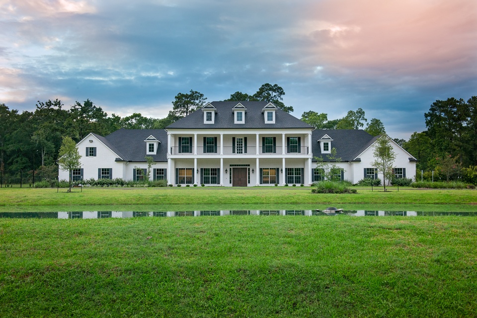 Elegant white mansion with a large green lawn and a pond reflecting the sky at sunset.