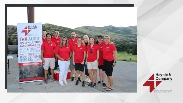 Group wearing red shirts standing outside near a Haynie promotional sign with mountains in the background.