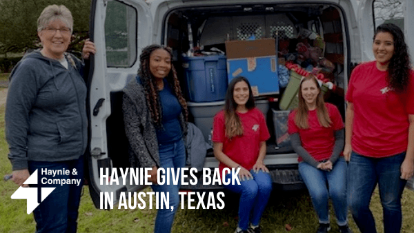 Group of women in red shirts volunteering with a van of donations in Austin, Texas.