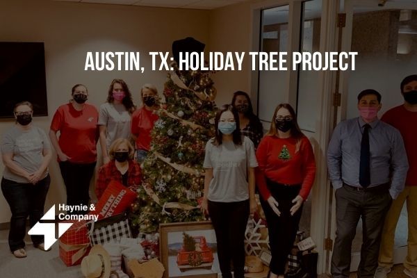 Group of people by decorated tree for Austin TX Holiday Tree Project, Haynie logo visible.
