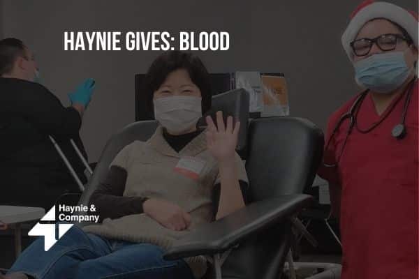 Haynie employee participating in a blood donation drive, seated and waving, with nurse in red Santa hat.