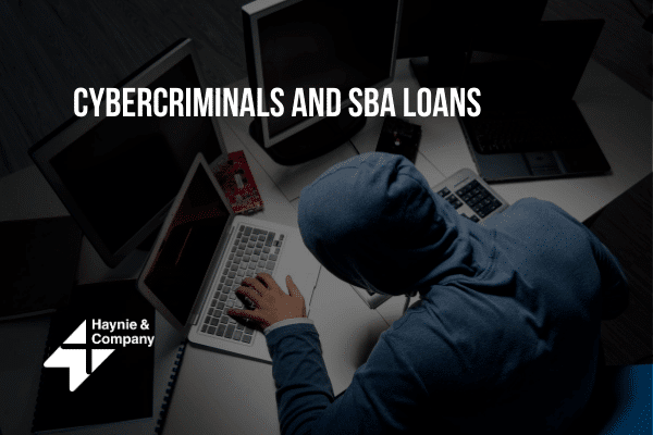Cybercriminal in a hoodie using laptops, with text Cybercriminals and SBA Loans and Haynie logo.