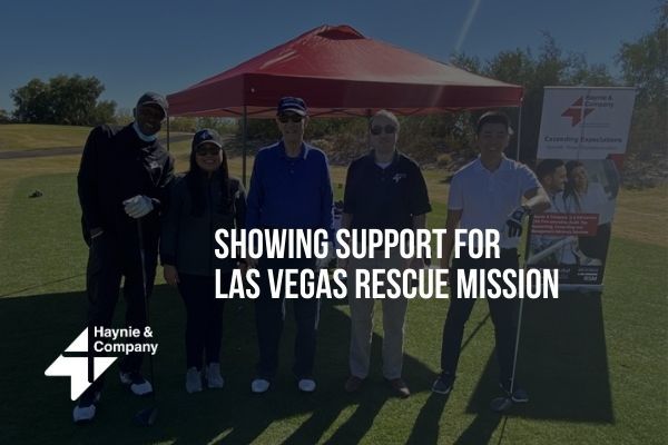 Golf event showing support for Las Vegas Rescue Mission with Haynie banner in the background.