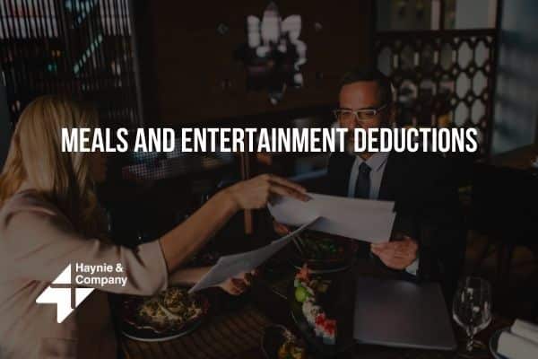 Two people reviewing documents over dinner, discussing meal and entertainment deductions. Haynie logo visible.