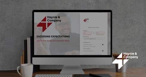 Computer screen displaying Haynie website, logo, coffee cup on desk.