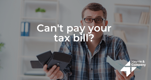 A person holding a wallet and bills with text Can't pay your tax bill? in a home setting.