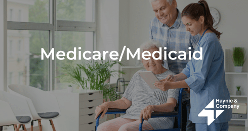 Older couple with a caregiver discussing Medicare/Medicaid options, Haynie logo.