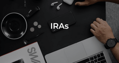 Workspace with IRAs text on phone alongside laptop, coins, stylus, and headphones.