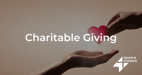 Charitable Giving: A hand offers a red heart to another hand, symbolizing donation and kindness. Haynie logo.