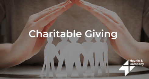 Hands forming a roof over paper figures with Charitable Giving text.