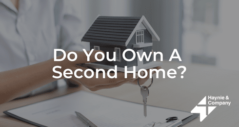 Person holding a model house and keys with text Do You Own A Second Home? and Haynie logo.