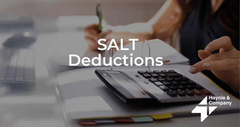 Person calculating SALT deductions with calculator, pen, and notebook.