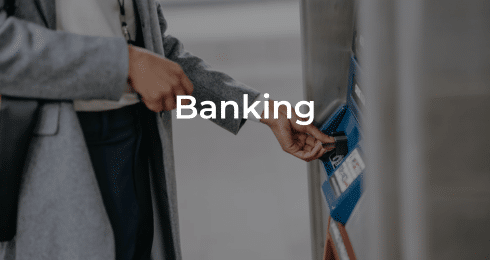 A person using an ATM for banking transactions, wearing a gray coat.