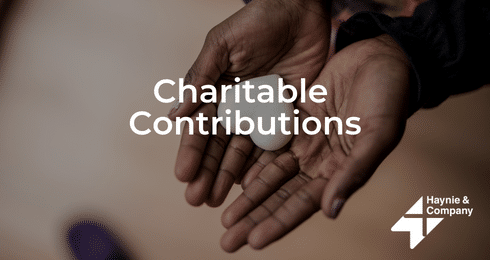 Hands holding a heart-shaped item, text Charitable Contributions, Haynie logo.