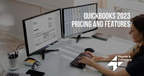 QuickBooks 2023 pricing and features displayed on dual monitors in office setting.