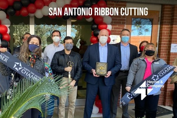 Group of people at San Antonio ribbon cutting event with scissors and balloons.