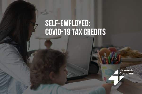Self-employed woman working on laptop with child nearby, COVID-19 tax credits info, Haynie services.