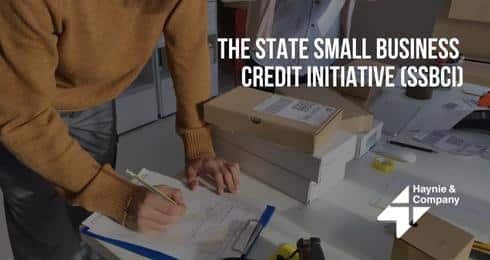 A person writing on a clipboard beside packages, text: The State Small Business Credit Initiative (SSBCI).