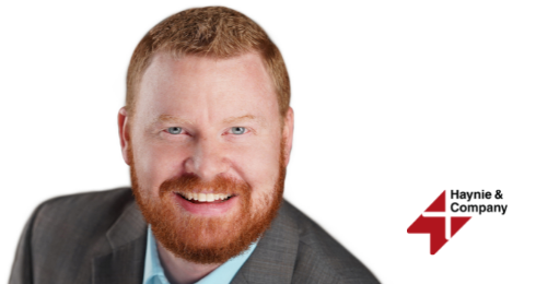 A smiling man in a suit with the Haynie logo on a white background.