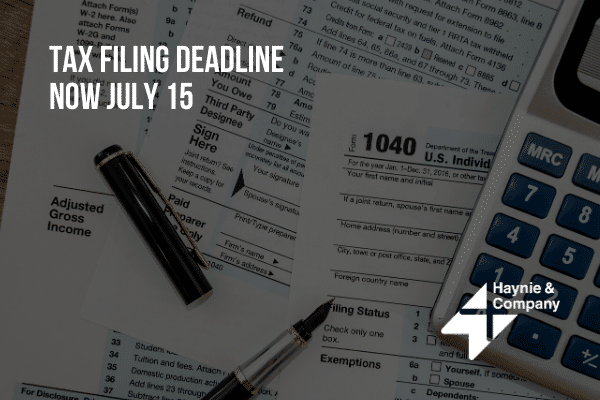 Tax filing deadline extended to July 15, forms, pen, and calculator on a desk.