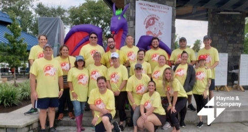 Group of people in yellow shirts posing at an outdoor event with an inflatable dragon in the background.