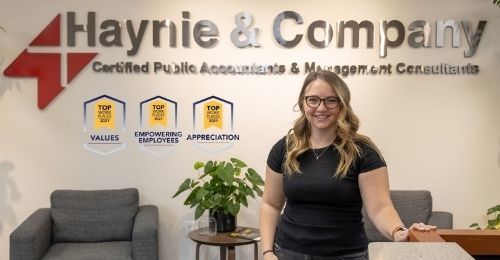 Woman standing in Haynie office, smiling, with award plaques on the wall in the background.