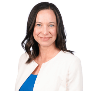 A woman in a white blazer and blue top smiling against a white background.