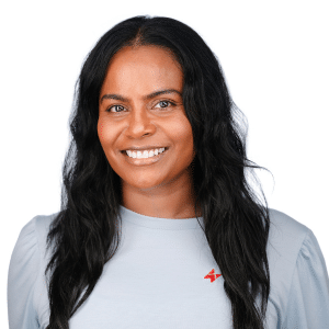 A smiling person with long hair wearing a gray shirt with a logo on a white background.