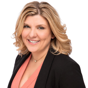Smiling woman with blonde hair in black blazer and coral top against white background.