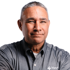 A man in a grey shirt with a Hayn logo, posing confidently against a white background.