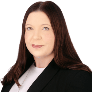 A woman with long brown hair in a black blazer against a white background.