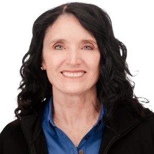 Woman smiling with dark hair, wearing a blue shirt and black jacket, against a white background.