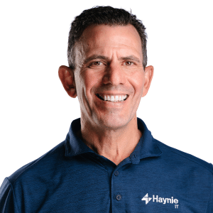A man in a blue Haynie IT shirt smiling at the camera with a white background.