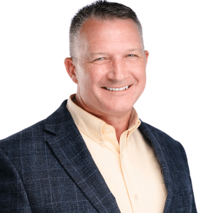 A man in a blazer and collared shirt smiles confidently against a white background.