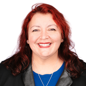 A woman with red hair smiling in a black blazer and blue shirt against a white background.