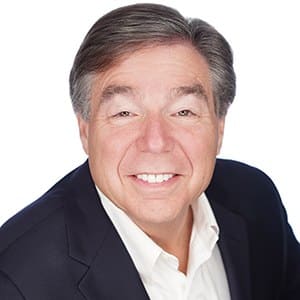 A smiling man in a suit against a white background.