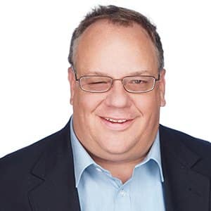 Man in glasses wearing a suit and light blue shirt, smiling at the camera.