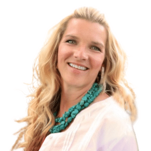 A woman with long blonde hair smiling, wearing a turquoise necklace and white top.