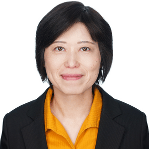 A person in a black blazer and yellow shirt smiling against a white background.