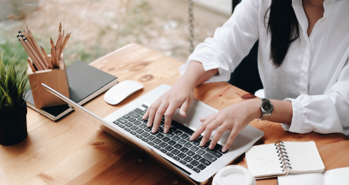 Woman typing on a laptop at a wooden desk with office supplies.