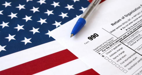 IRS Form 990 with pen on American flag background, tax document concept.