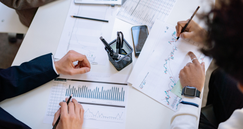 Business meeting with charts and graphs on table, hands holding pens, analyzing data.