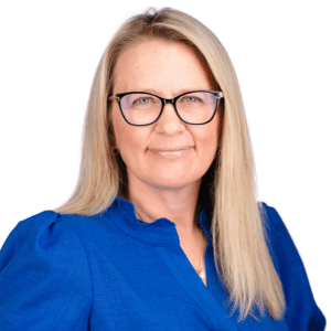 A woman in a blue blouse and glasses with a neutral expression against a white background.